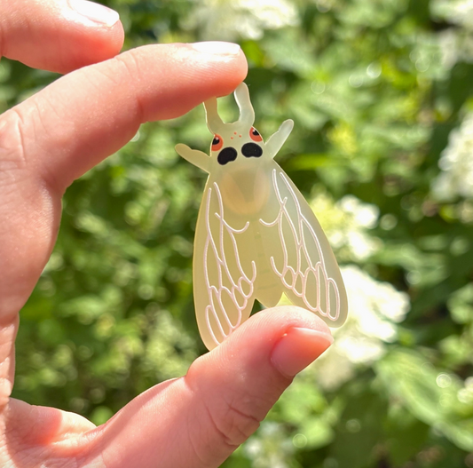 Hand holding a transparent insect-shaped object with a blurred green background