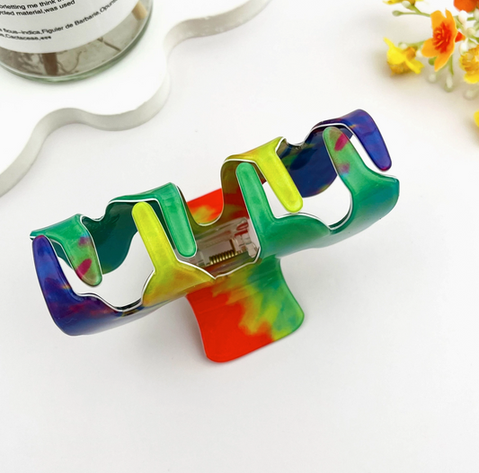 Colorful tie-dye hair clip on a white surface with flowers in the background