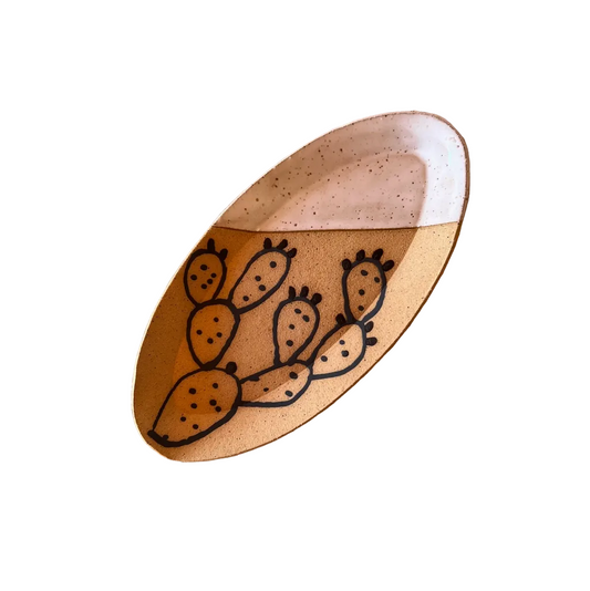 An oval ceramic plate with a hand-painted cactus design, displayed on a woven straw sun hat.