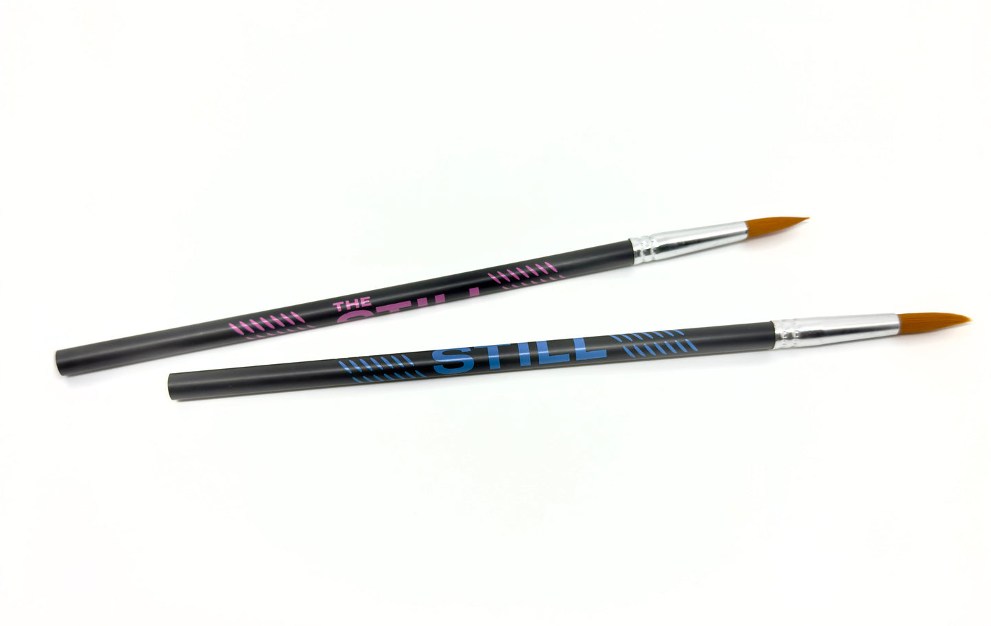 Two "The Still" branded pencils with paint brushes on one end