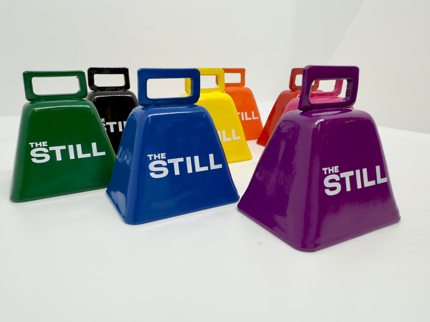 Colorful cowbells with 'The Still' branding on a white background