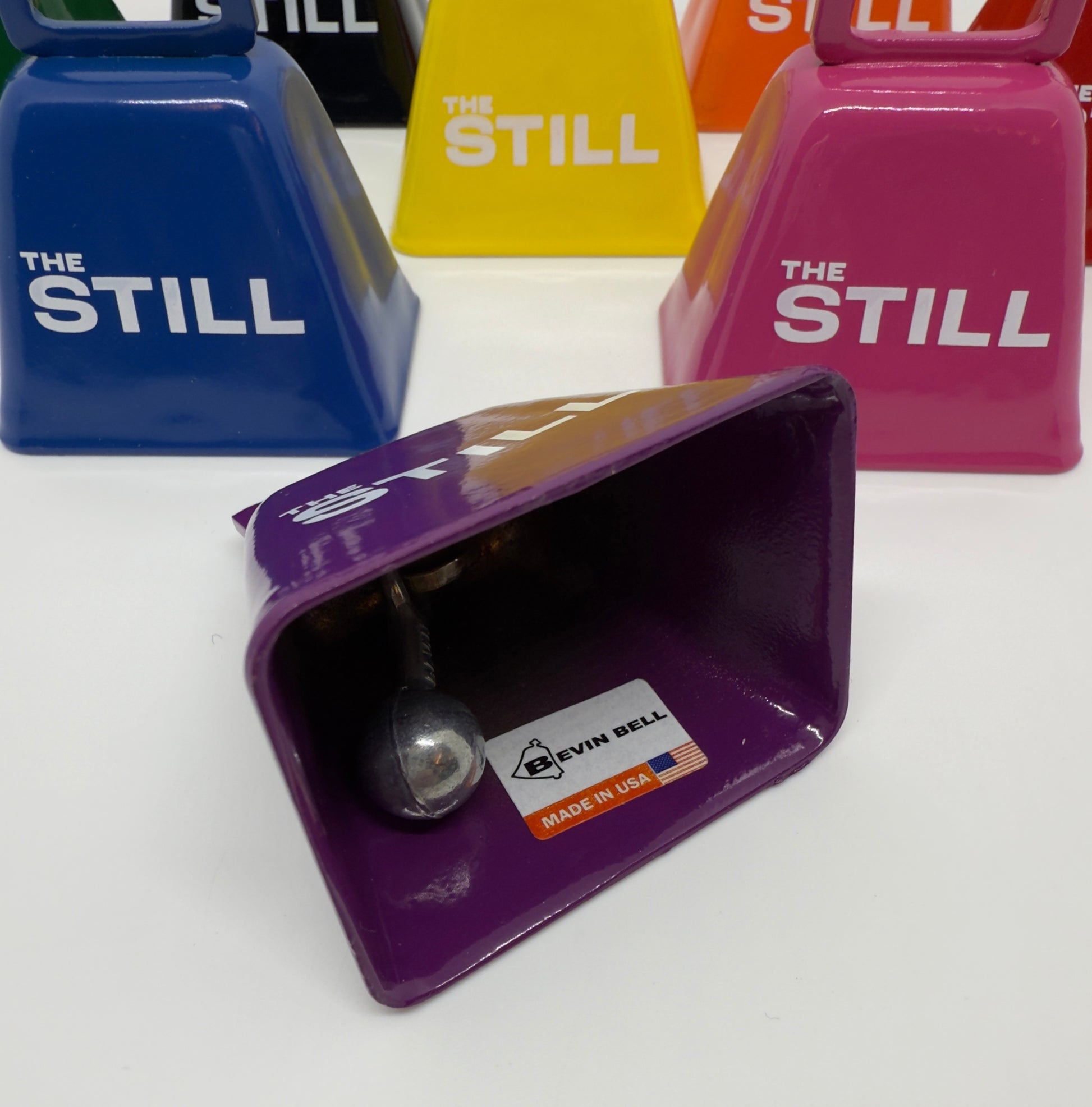 Colorful cowbells with 'The Still' branding on a white background