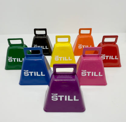 Colorful cowbells with 'The Still' branding on a white background