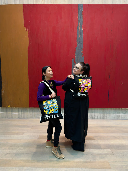 Two people standing in front of a large abstract painting with tote-paks.