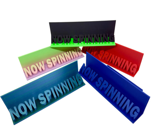 Four colorful acrylic spinning signs with 'NOW SPINNING' text on a white background