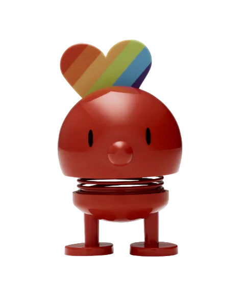 A colorful figurie with a round body and a rainbow-patterned heart on top, standing upright on a flat surface.