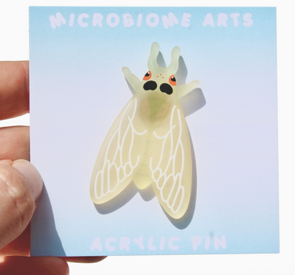 Acrylic pin of a cartoon-like insect held over a card with 'Microbiome Arts' branding.