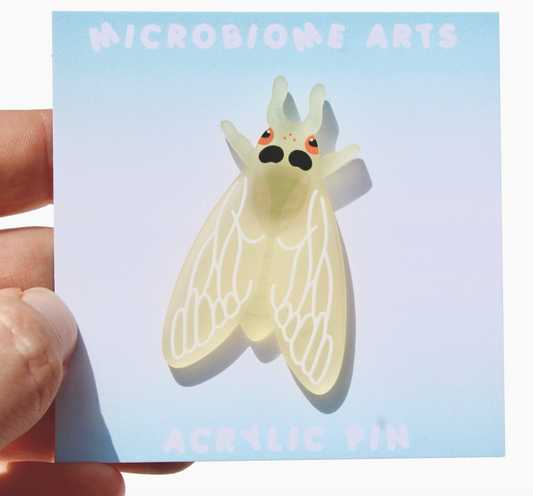 Acrylic pin of a cartoon-like insect held over a card with 'Microbiome Arts' branding.