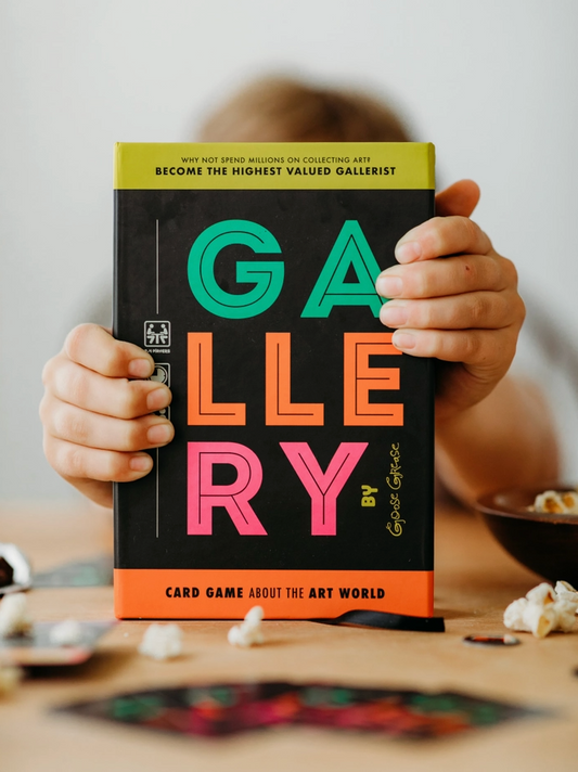 Person holding a card game box titled 'GALLERY' with colorful text.