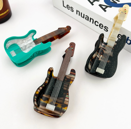 Three guitar-shaped hair clips on a white surface with a book in the background.