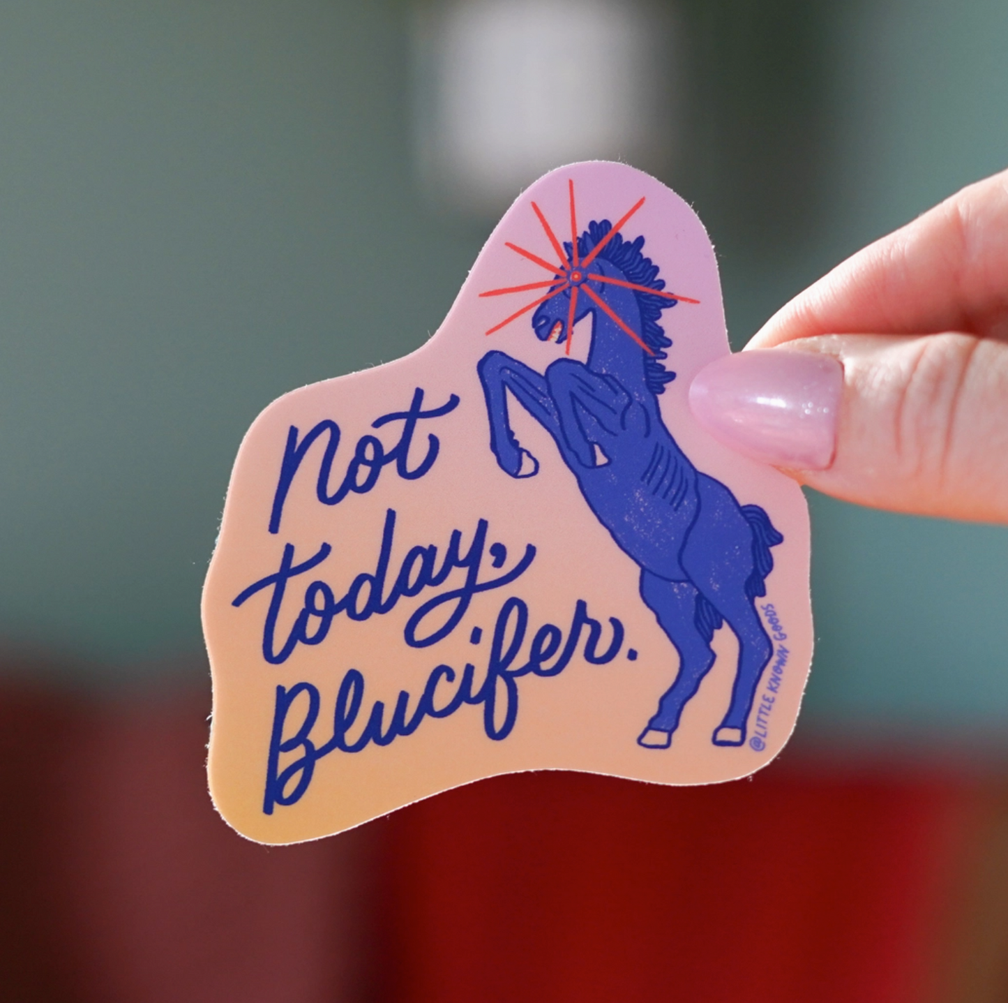 Sticker with a horse and text 'Not today, Blucifer' held by a hand against a blurred background