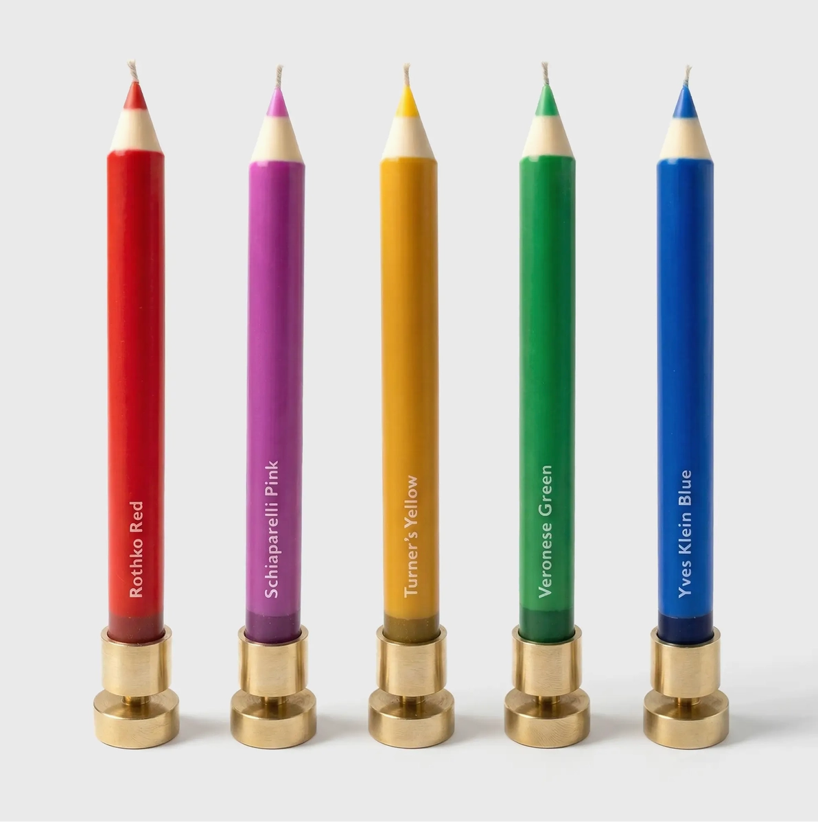 Five colorful candles with brass bases on a white background