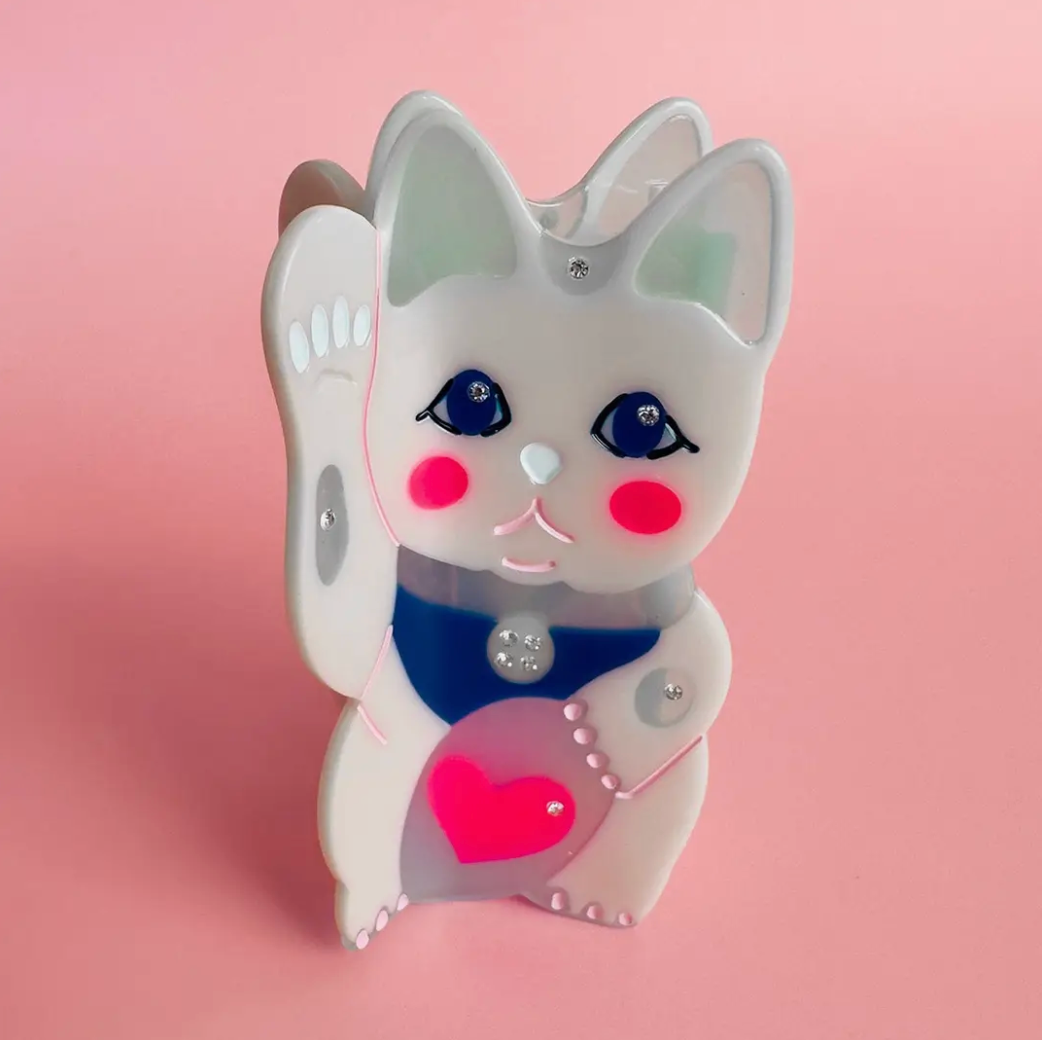 Cute cartoon-style lucky cat hair clip with a pink heart on a pink background