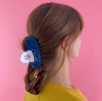 Person with a braid wearing a blue hair hair clip against a pink background