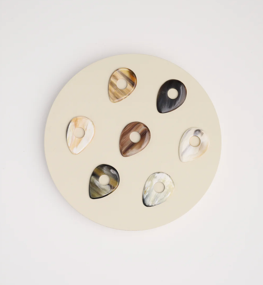 Set of horn guitar picks earrings on a round beige background.