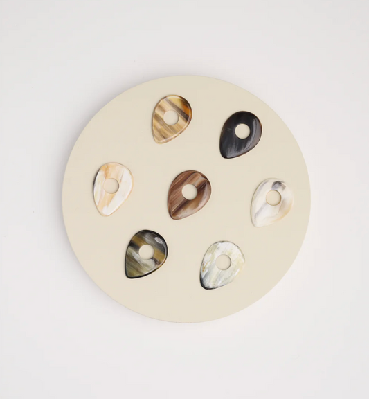 Set of horn guitar picks earrings on a round beige background.