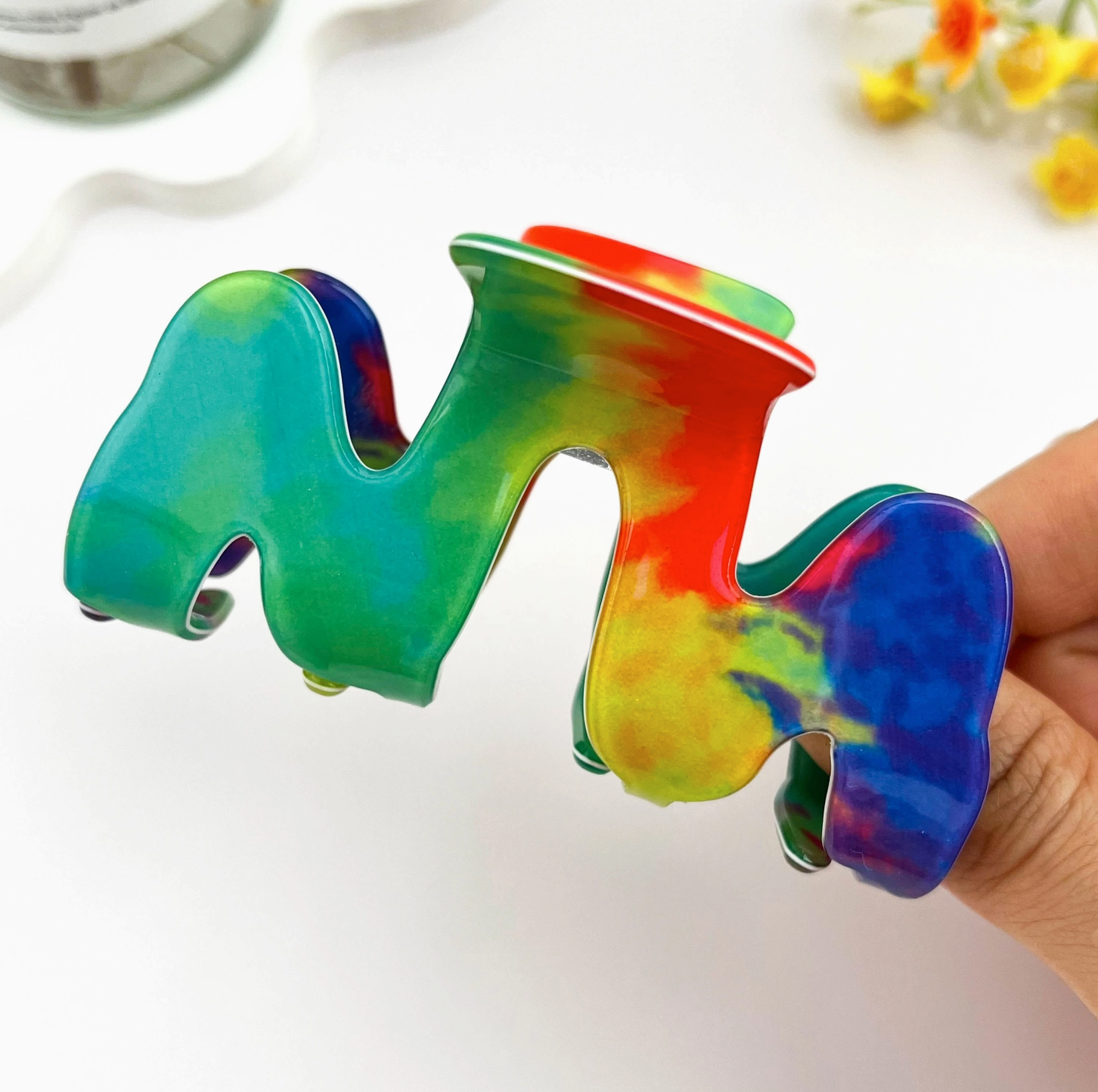 Colorful tie-dye letter 'M' held by a hand on a white background