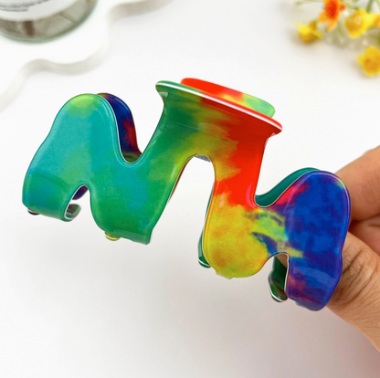 Colorful tie-dye letter 'M' held by a hand on a white background