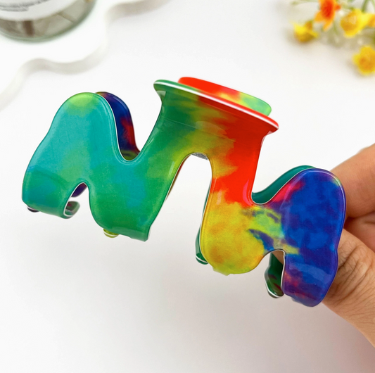 Colorful tie-dye letter 'M' held by a hand on a white background