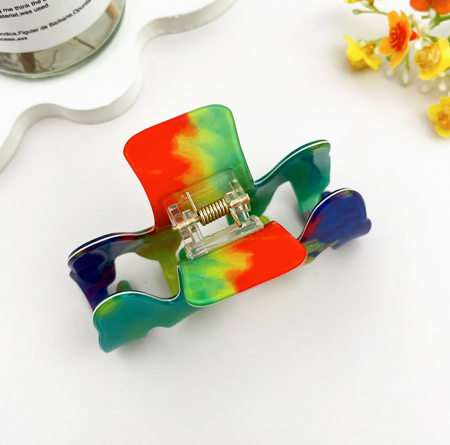 Colorful tie-dye hair clip on a white background with flowers and ribbon.