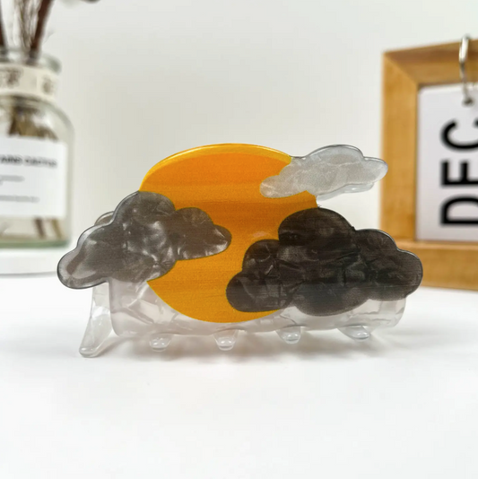 Decorative hair clip with orange center, black clouds, and clear base on a white surface.