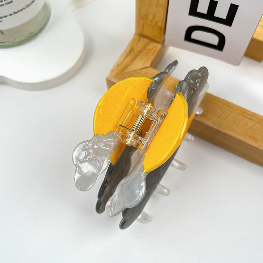 Close-up of a hair clip on a white surface with a wooden block in the background.