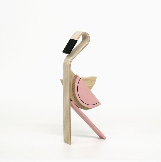 A modern wooden bird sculpture or decorative object with layered plywood construction, featuring a natural wood body, a pink wing, and a black accent on the beak, set against a plain white background.