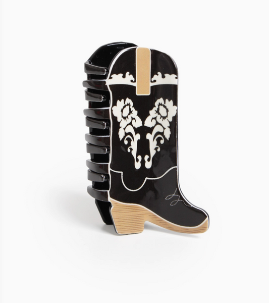 A glossy black cowboy boot-shaped hair claw clip with white western-style floral scrollwork and beige accents, shown on a clean white background.