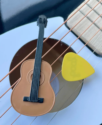 Small model of a guitar with a yellow pick on a white surface