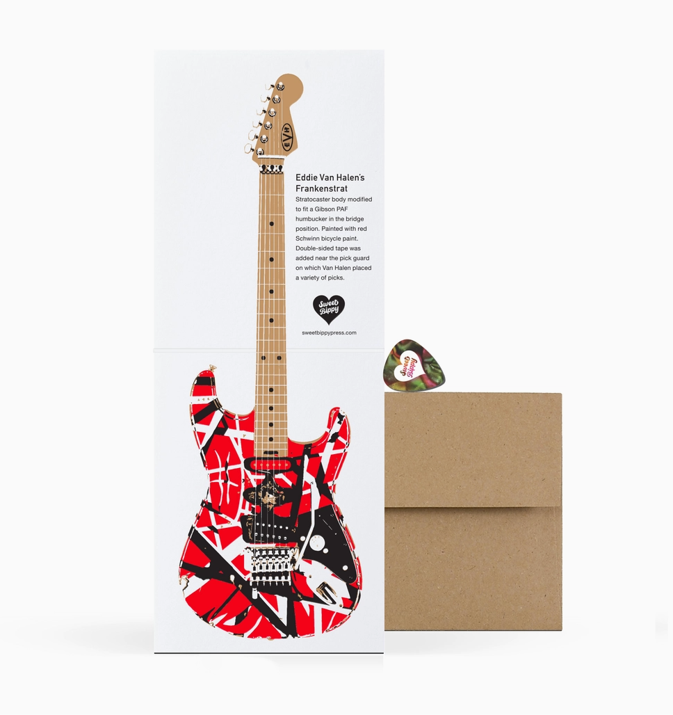 Guitar-shaped card with red and black design, envelope, and pick on a white background