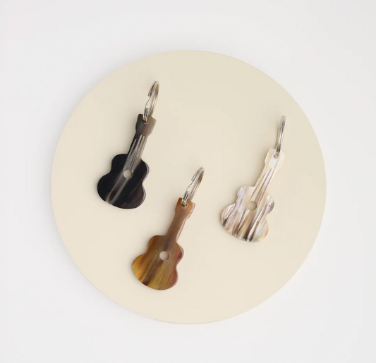 Three guitar-shaped keychains on a round beige pad with a white background