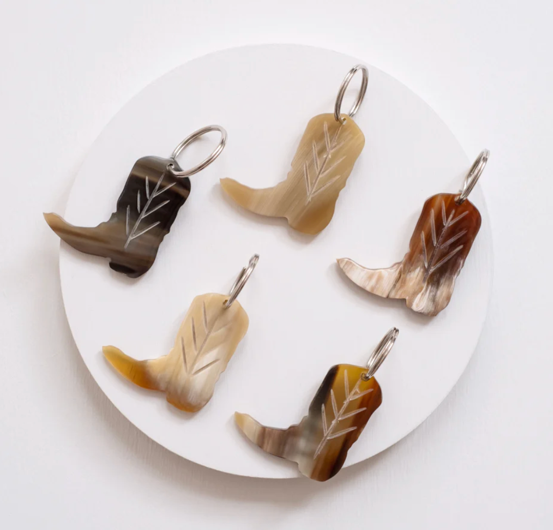 Five cowboy boot-shaped keychains on a white circular stand with a white background