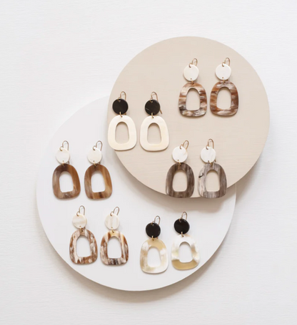 Earrings on a white and beige circular stand against a light gray background