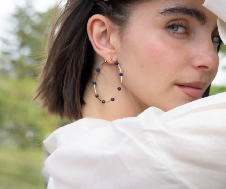 Woman wearing hoop earrings with blue beads, outdoors.