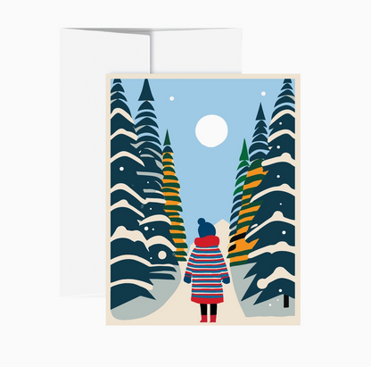 A square greeting card with a white envelope behind it, featuring a stylized winter forest illustration. The card shows a person in a red, blue, and white striped coat standing on a snowy path between tall pine trees under a pale blue sky and a white moon.
