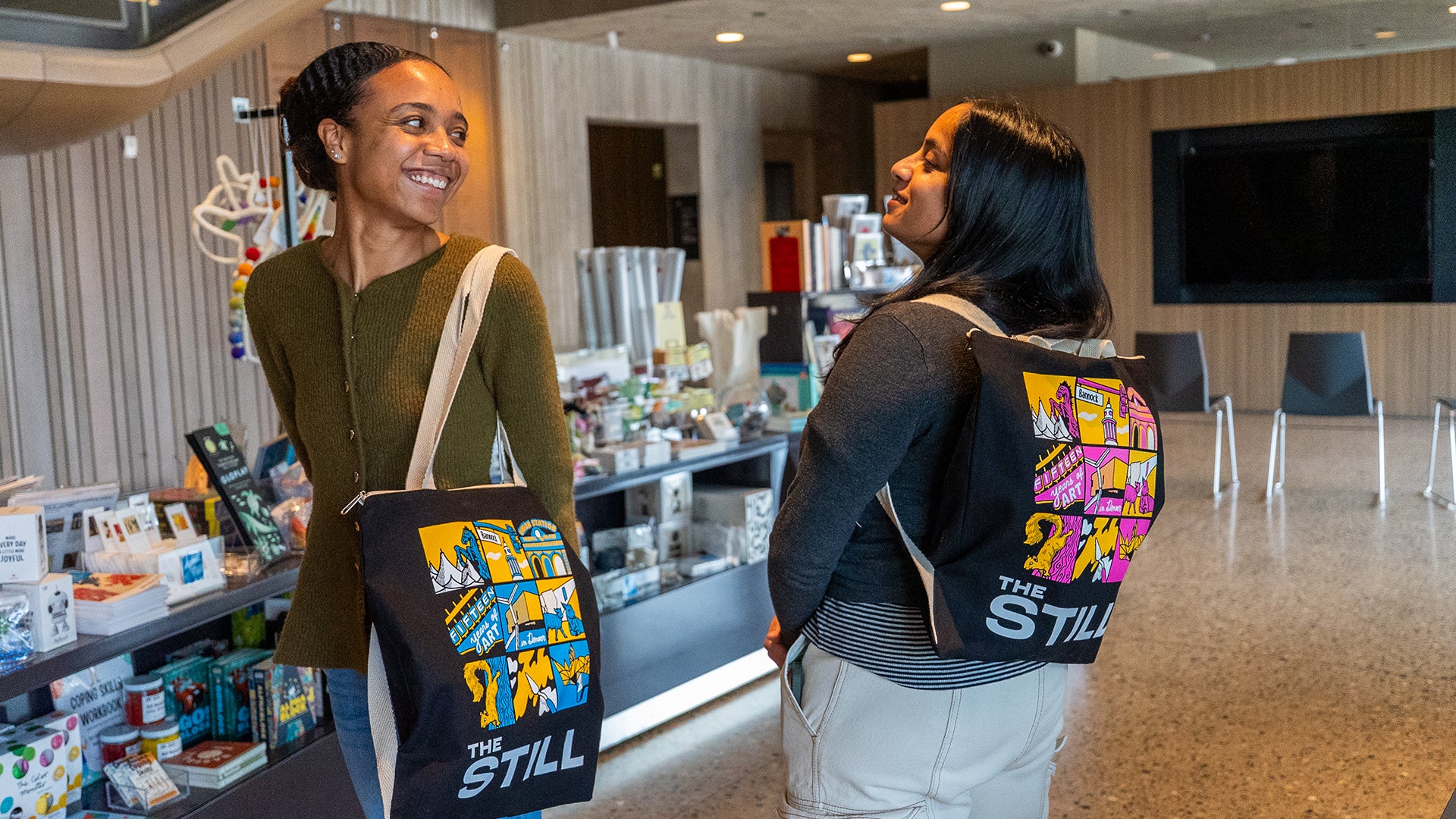 Two women with colorful bags standing in a store.